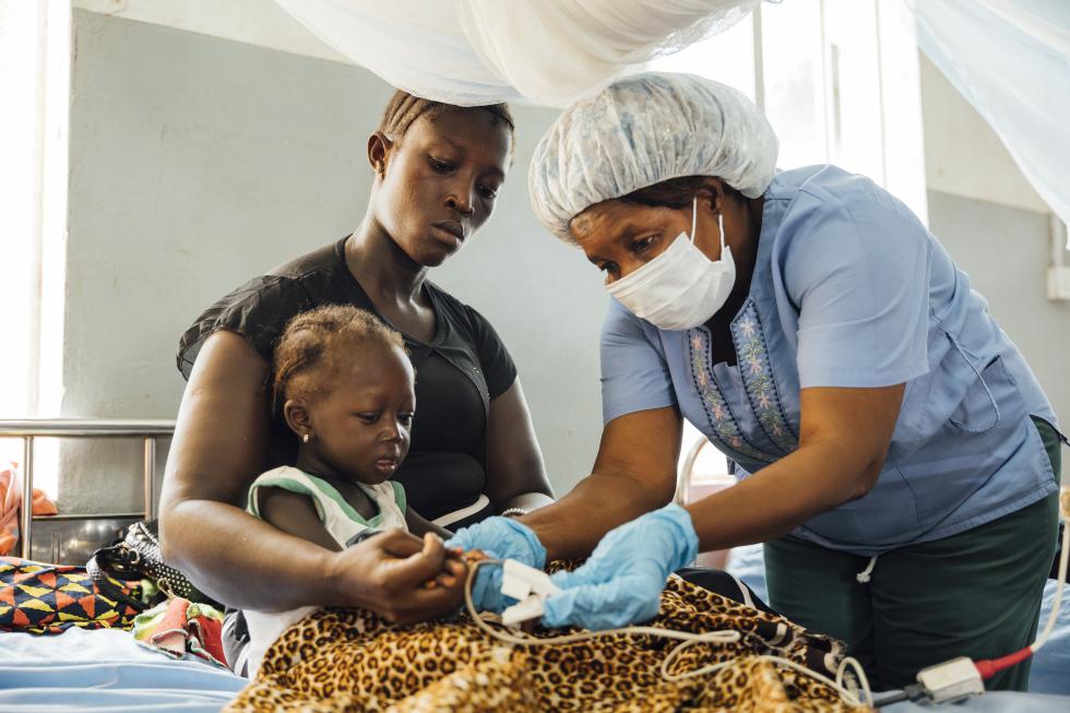 Nurse in MSF-supported Magburaka District Hospital is attending to a young patient Memunatu who has severe malaria. Memunatu is seen sitting with her mother Mamusu Kargbo. 